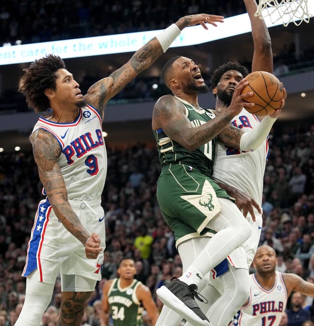 Milwaukee Bucks guard Damian Lillard (0) draws a foul from Philadelphia 76ers center Joel Embiid (21) while also being defended by guard Kelly Oubre Jr. (9) during the second half of their regular season opener Thursday, October 26, 2023 at Fiserv Forum in Milwaukee, Wisconsin. The Milwaukee Bucks beat Philadelphia 76ers 118-117.