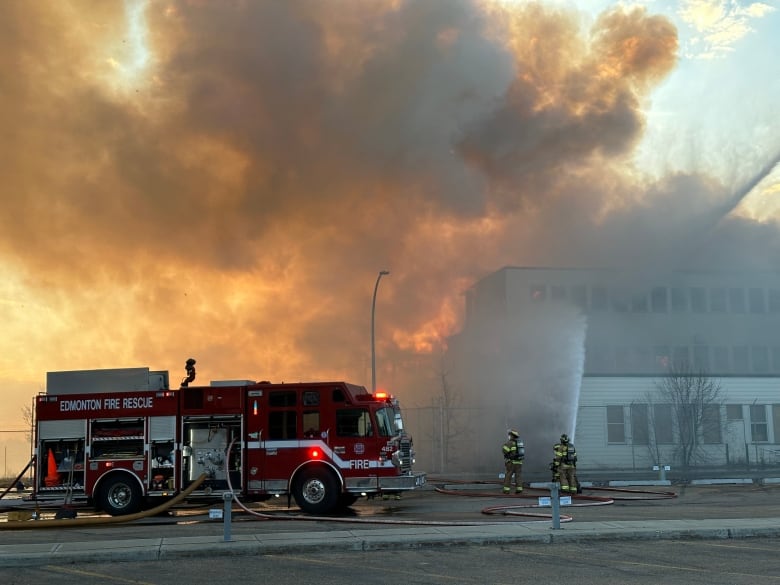 A firetruck and firefighters in front of a building on fire.