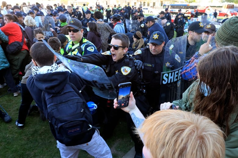 A police officer with yells while hitting a protester with his shield amid clashes between police and other protesters. 