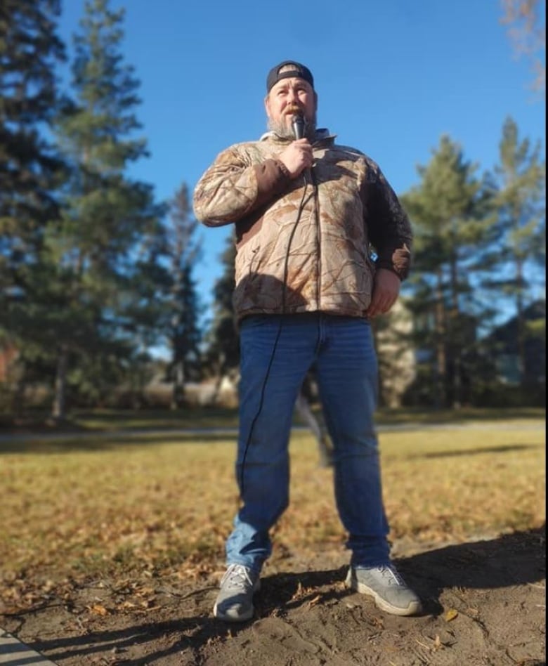 A man stands outside holding a microphone. 