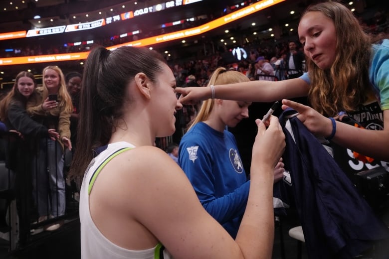 A woman basketball player signs autographs.