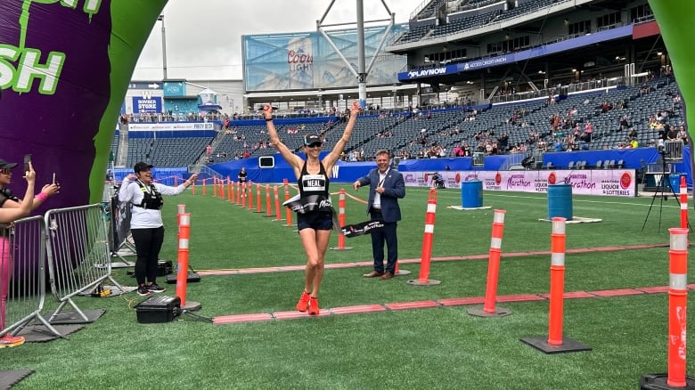 A woman crosses a finish line with her arms raised in the air.