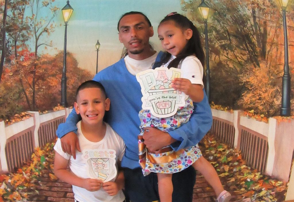 Two children hold Father's Day cards while visiting their incarcerated family member while posing for a photo.