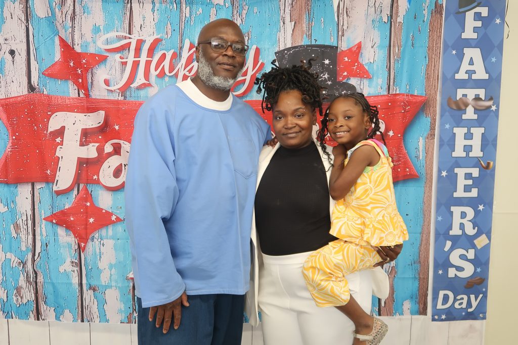 An incarcerated man, a woman and a young child during a CDCR Father's Day visiting event at California Men's Colony.