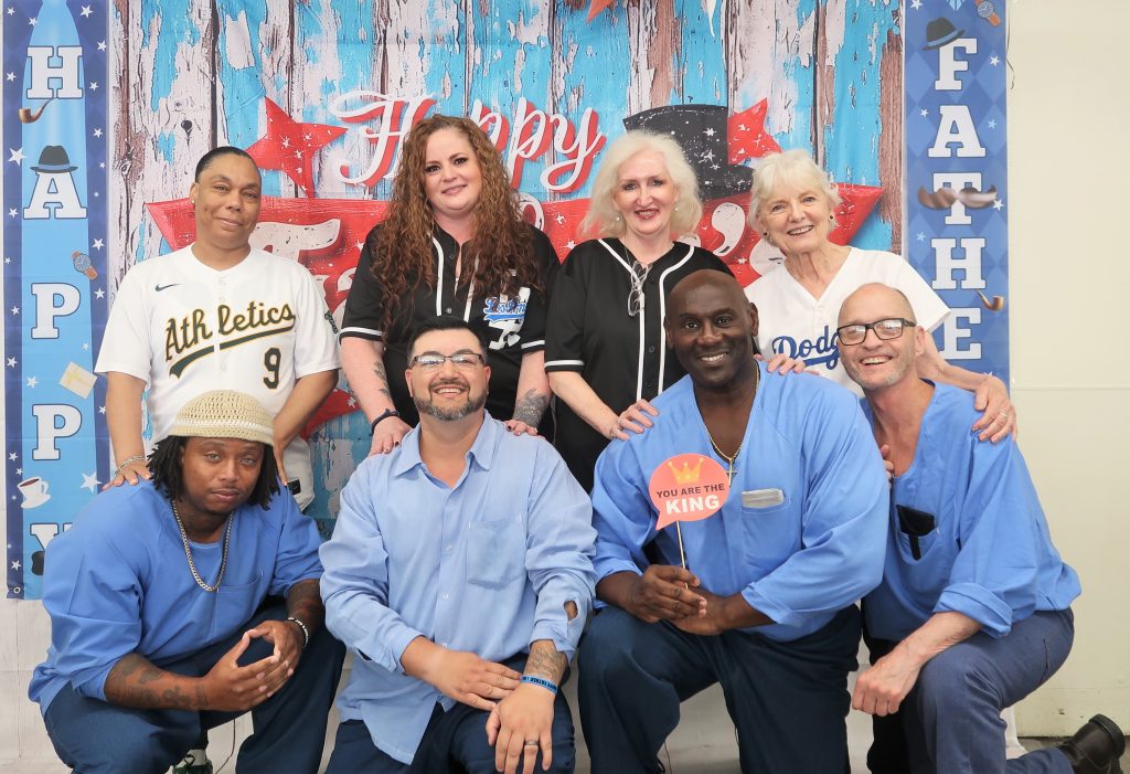 A group of incarcerated people and their visiting family members wearing baseball jerseys.