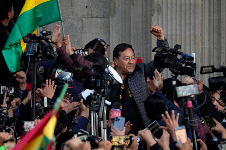 Bolivian President Luis Arce raises a clenched fist surrounded by supporters and media, outside the government palace in La Paz, Bolivia, 