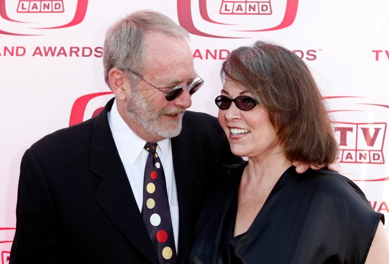 Two people wearing sunglasses smile while embracing.