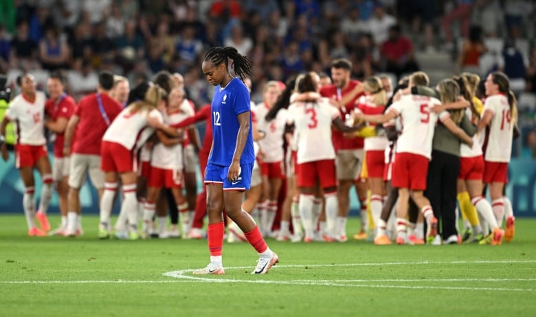 A female player looks dejected as she walks past a team of celebrating players.