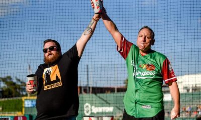 Competitive eater Joey Chestnut, right, celebrates after eating 13 olive burgers in five minutes before a minor league baseball game at Jackson Field in Lansing, Michigan on Aug. 10, 2023.