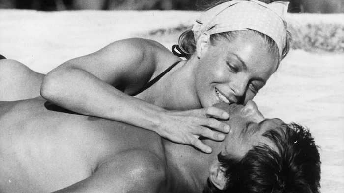 Romy Schneider étendue sur Alain Delon, allongé sur le sable.