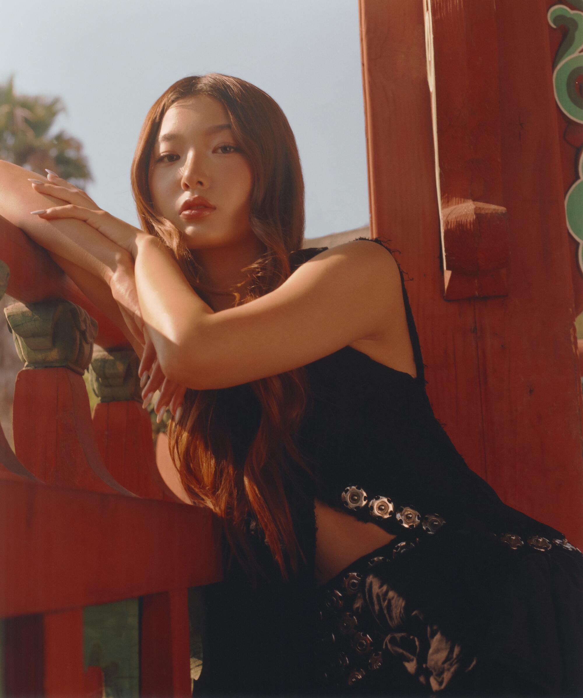 Yoonchae poses under a gazebo with Korean architecture.