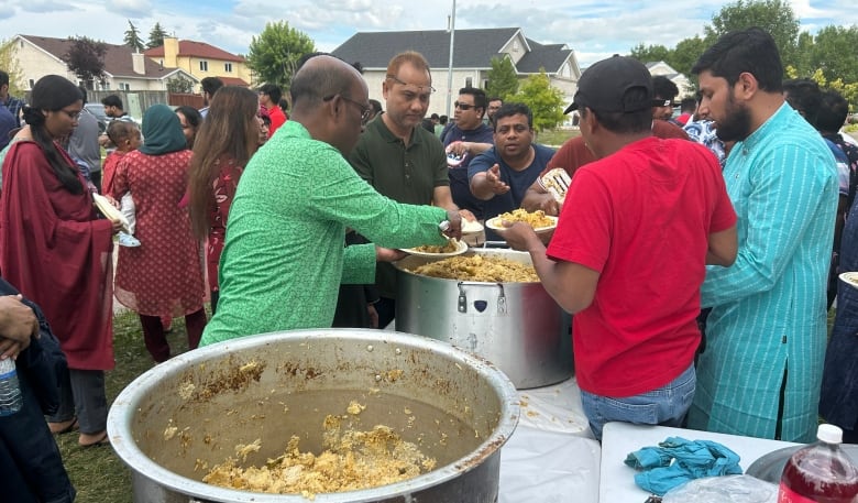 Man in green shirt scoops food out of a large pot amid a crowd.