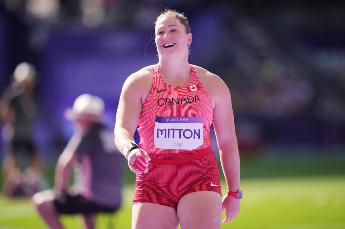 Sarah Mitton smiles while wearing a pink and red athletics singlet 