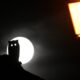 the silhouette of a halloween owl decoration sits in front of the white full moon. On the right in the foreground, a yellow sreat lamp.