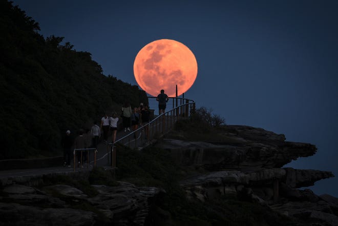 A supermoon rises behind people walking on a headland near Sydney's Bondi Beach on October 17, 2024.