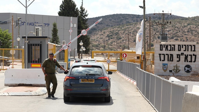 Un soldat debout à côté d'une voiture à l'entrée d'une base militaire sécurisée.