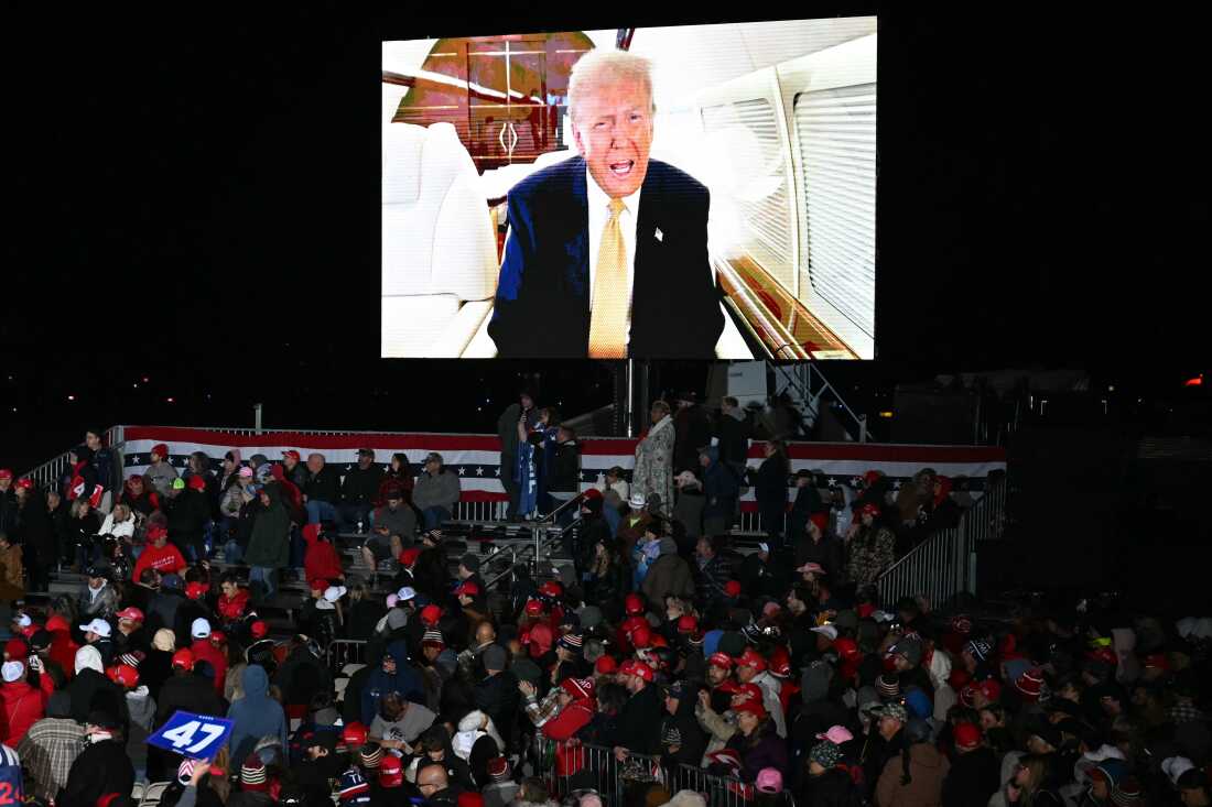 Former President Donald Trump sends a personal message on the jumbotron informing attendees that he would be three hours late for a campaign rally in Traverse City, Michigan, on Friday.