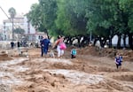 TOPSHOT - Family members walk in a street covered in mud in a flooded area in Picanya, near Valencia, eastern Spain, on October 30, 2024. Floods triggered by torrential rains in Spain's eastern Valencia region has left 51 people dead, rescue services said on October 30. (Photo by Jose Jordan / AFP) (Photo by JOSE JORDAN/AFP via Getty Images)