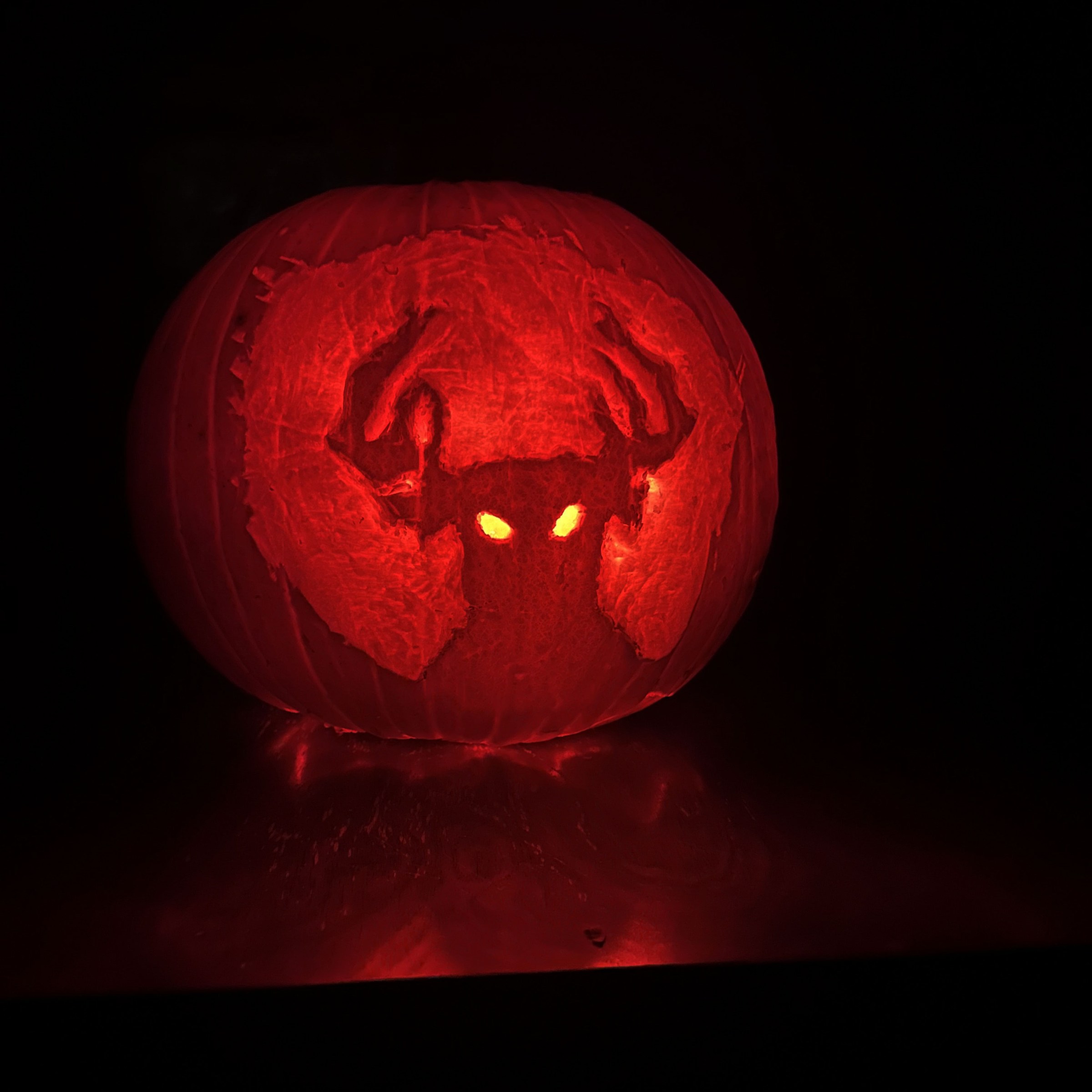 A pumpkin is carved with the silhouette of a person with elk horns and glowing eyes. The background glows softly.  