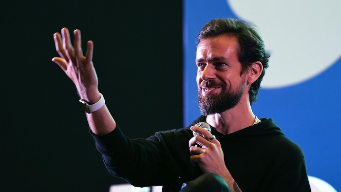 Jack Dorsey parle sur scène avec un micro lors d'une conférence devant le logo de Twitter.