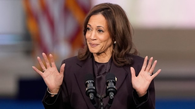 Kamala Harris devant un lutrin, elle lève les mains dans les airs.