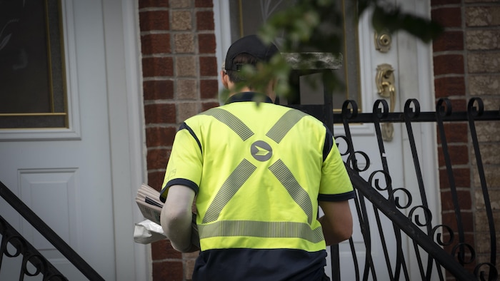 Un facteur de Postes Canada livre du courrier en marchant.