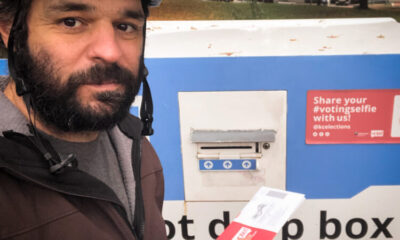 Selfie of the author wearing a bike helmet about to put a ballot into a drop box with gas works park in the background.