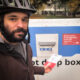 Selfie of the author wearing a bike helmet about to put a ballot into a drop box with gas works park in the background.