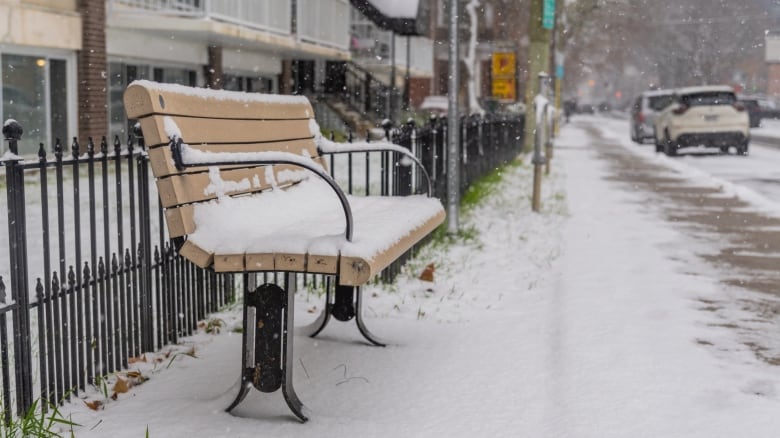 Snow coats a sidewalk and bench in a city.