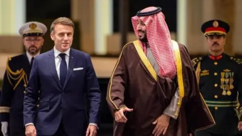 Shutterstock Emmanuel Macron walks next to Saudi Crown Prince Mohammed bin Salman (R) at Al-Yamamah Palace in Riyadh, Saudi Arabia, with two men in military uniforms walking behind them