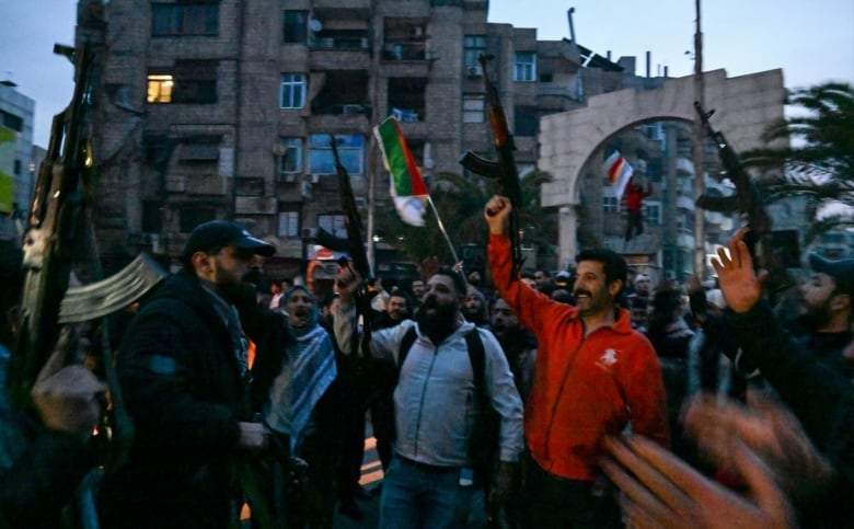 A crowd of people raise assault rifles and flags during a public celebration.