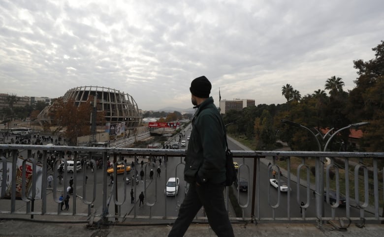 A pedestrian crosses a bridge as cars and other people navigate a road below.