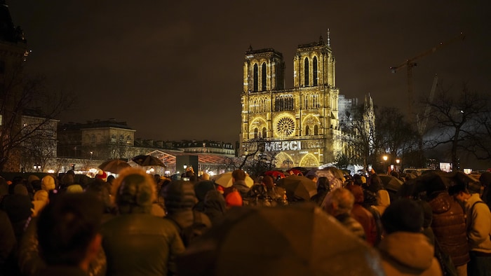 La cathédrale illuminée de teintes dorées est entourée d'une foule. 