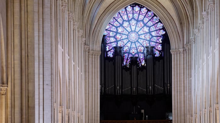 Un très grand orgue sombre est situé devant la rosace d'un vitrail.