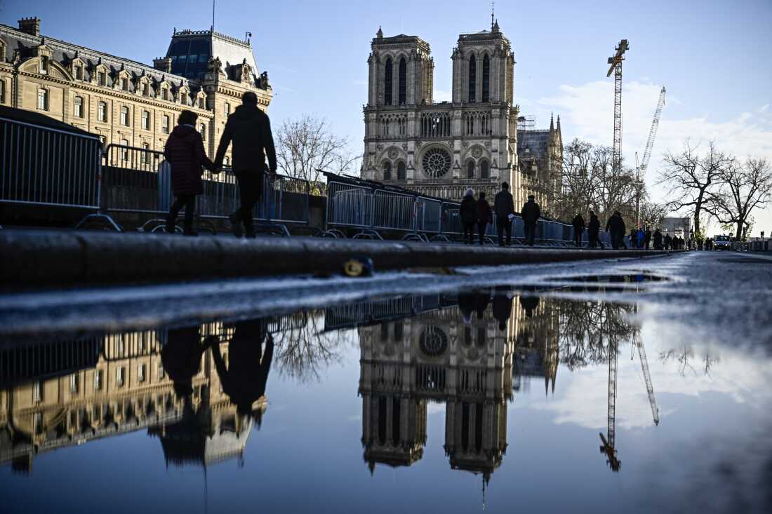 TOPSHOT - Pedestrians pass by the security barriers and fences placed around the Notre-Dame de Paris cathedral on the eve ahead of its official reopening after more than five-year of reconstruction work following the April 15, 2019 fire, in Paris, on December 6, 2024. The Notre-Dame Cathedral is set to re-open early December 2024, with a planned weekend of ceremonies on December 7 and 8, 2024, five years after the 2019 fire which ravaged the world heritage landmark and toppled its spire. Some 250 companies and hundreds of experts were mobilised for the five-year restoration costing hundreds of millions of euros. (Photo by JULIEN DE ROSA / AFP) (Photo by JULIEN DE ROSA/AFP via Getty Images)