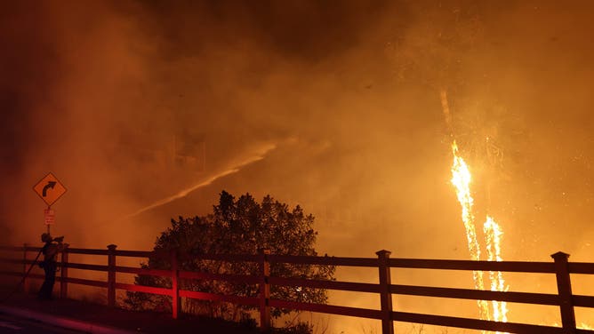 MALIBU, CALIFORNIA - DECEMBER 10: A firefighter sprays water as the Franklin Fire burns near a building on December 10, 2024 on Malibu, California. The wildfire has scorched 1,800 acres near Pepperdine University prompting evacuations along the coast amid high winds with some structures destroyed. (Photo by Mario Tama/Getty Images)