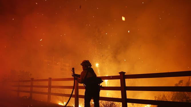 MALIBU, CALIFORNIA - DECEMBER 10: A firefighter pulls a water hose as the Franklin Fire burns near a building on December 10, 2024 in Malibu, California. The wildfire has scorched 1,800 acres near Pepperdine University prompting evacuations along the coast amid high winds with some structures destroyed. (Photo by Mario Tama/Getty Images)