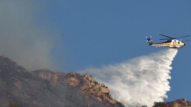 A firefighting helicopter drops water as the Franklin Fire continues to burn on December 10, 2024 in Malibu, California. 