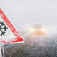 Snowfall warning sign surround by snow and a picture of a car with its headlights on on a highway.