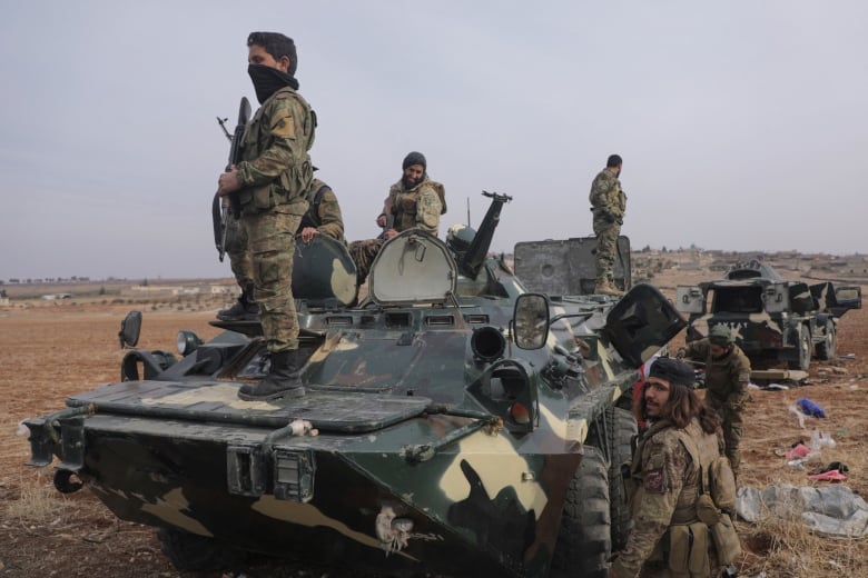 Armed fighters in military garb stand atop and around a military vehicle.