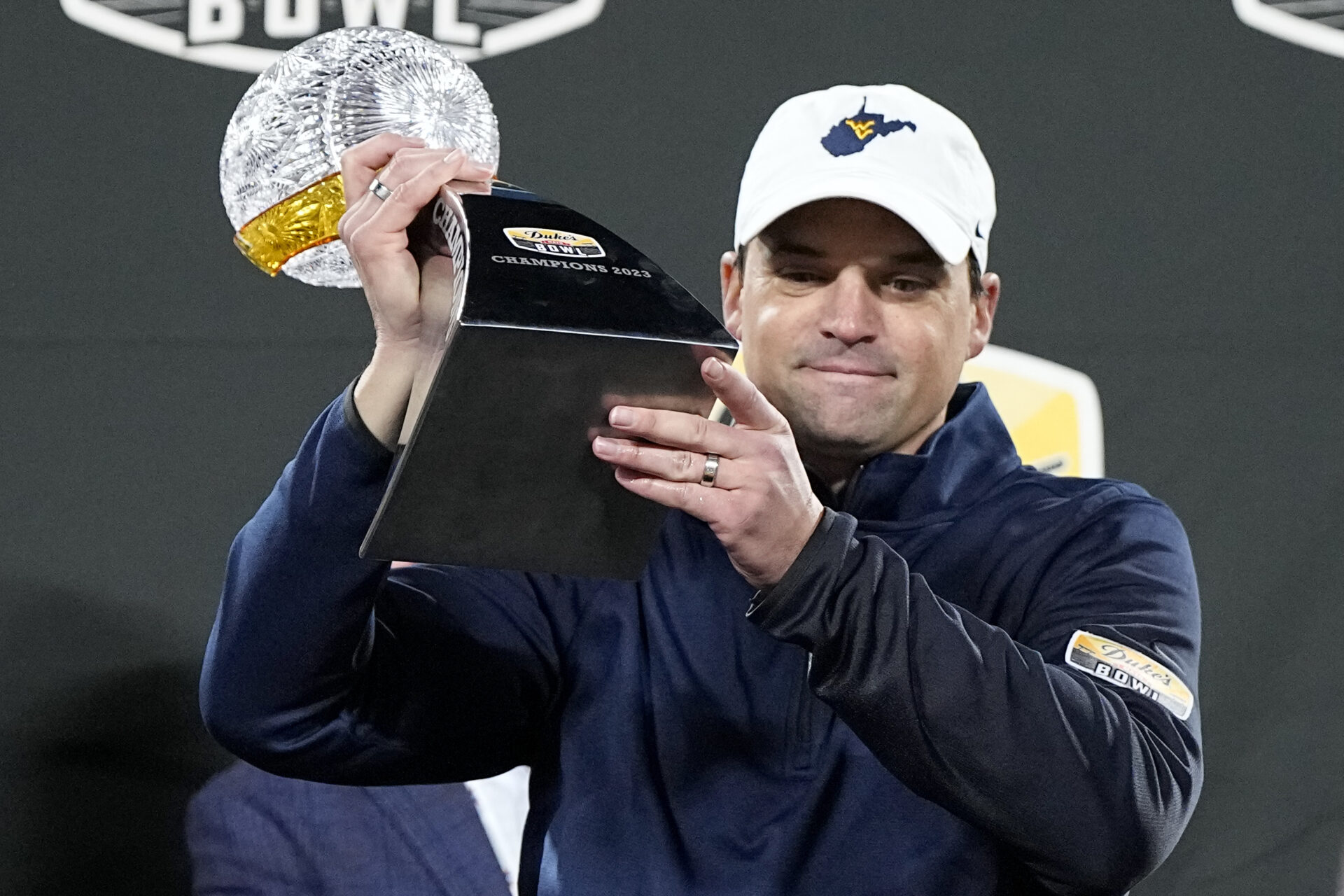 A man is wearing a ball cap featuring the shape of West Virginia.