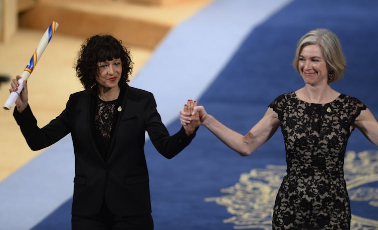 two women raise grasped hands and one holds a rolled up award