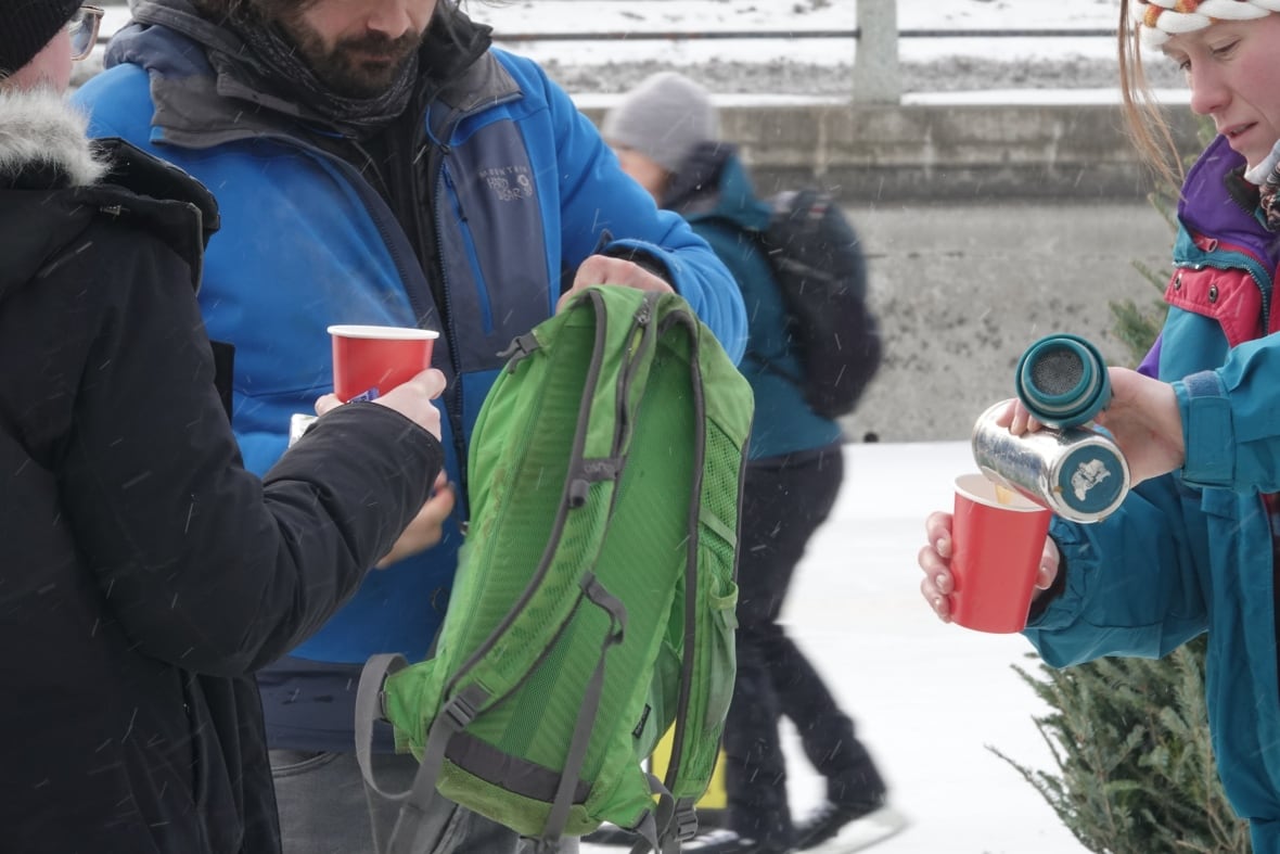 Three people share a hot beverage on an outdoor skating rink.