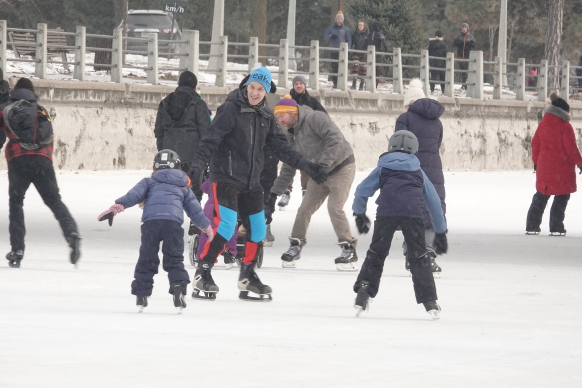 An adult smiles at a child skating on an outdoor ice rink.