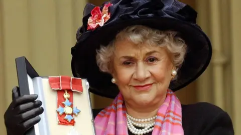 PA Media Dame Joan Plowright holding up her medal after being made a dame in 2004